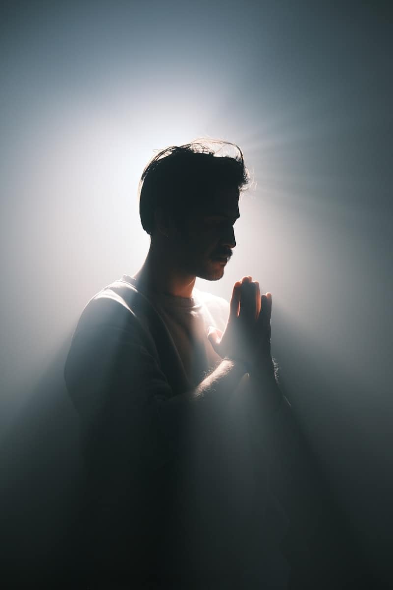Man standing in soft light with hands pressed in reflection, symbolising how tarot helps people navigate spiritual shifts and real-life turning points.