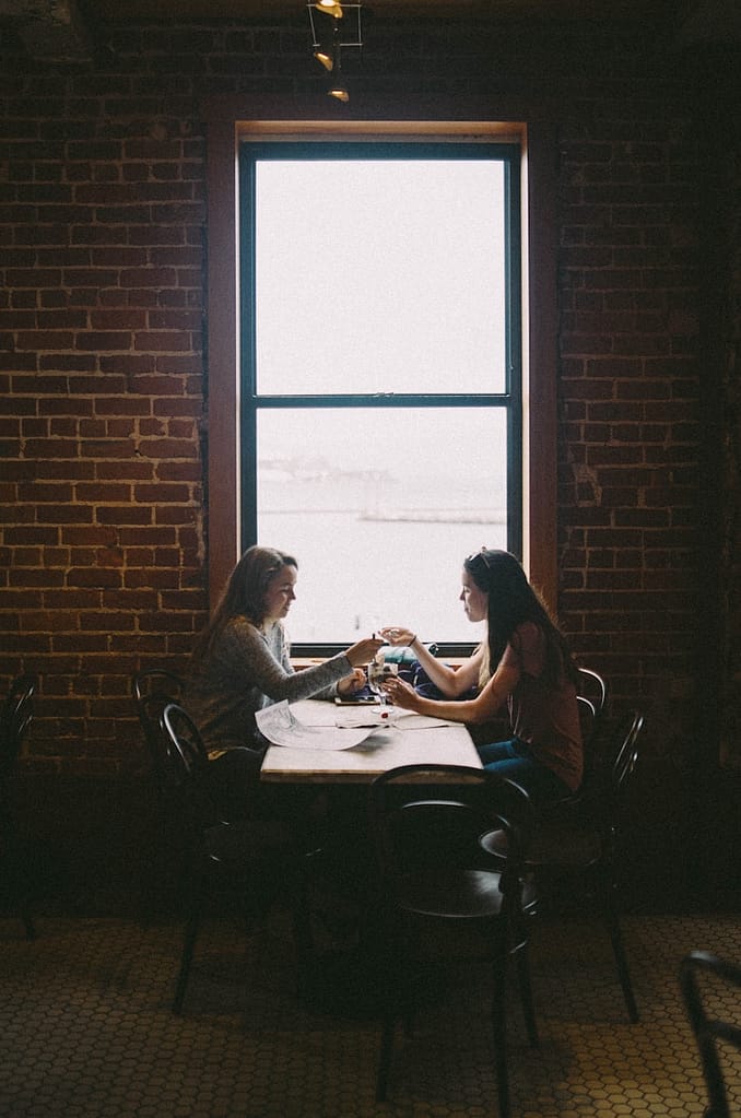 “Two people sitting across from each other at a table, representing a tarot reader and client setting boundaries and discussing spiritual work and money