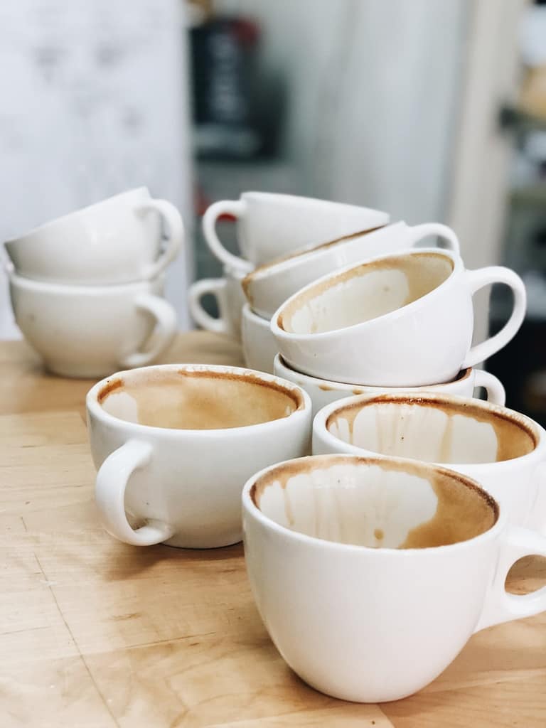 A pile of empty, stained coffee cups stacked on a wooden table, symbolising feeling emotionally drained and in need of a reset.