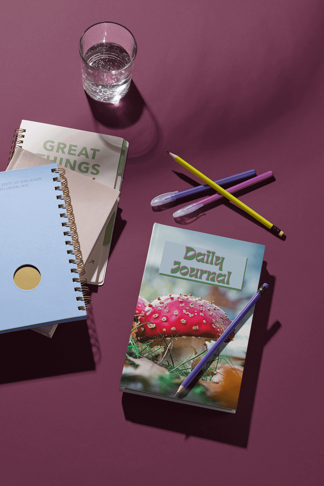 A set of colourful journals and pens next to a glass of water on a pink surface, representing journalling as a way to emotionally release and process emotions.