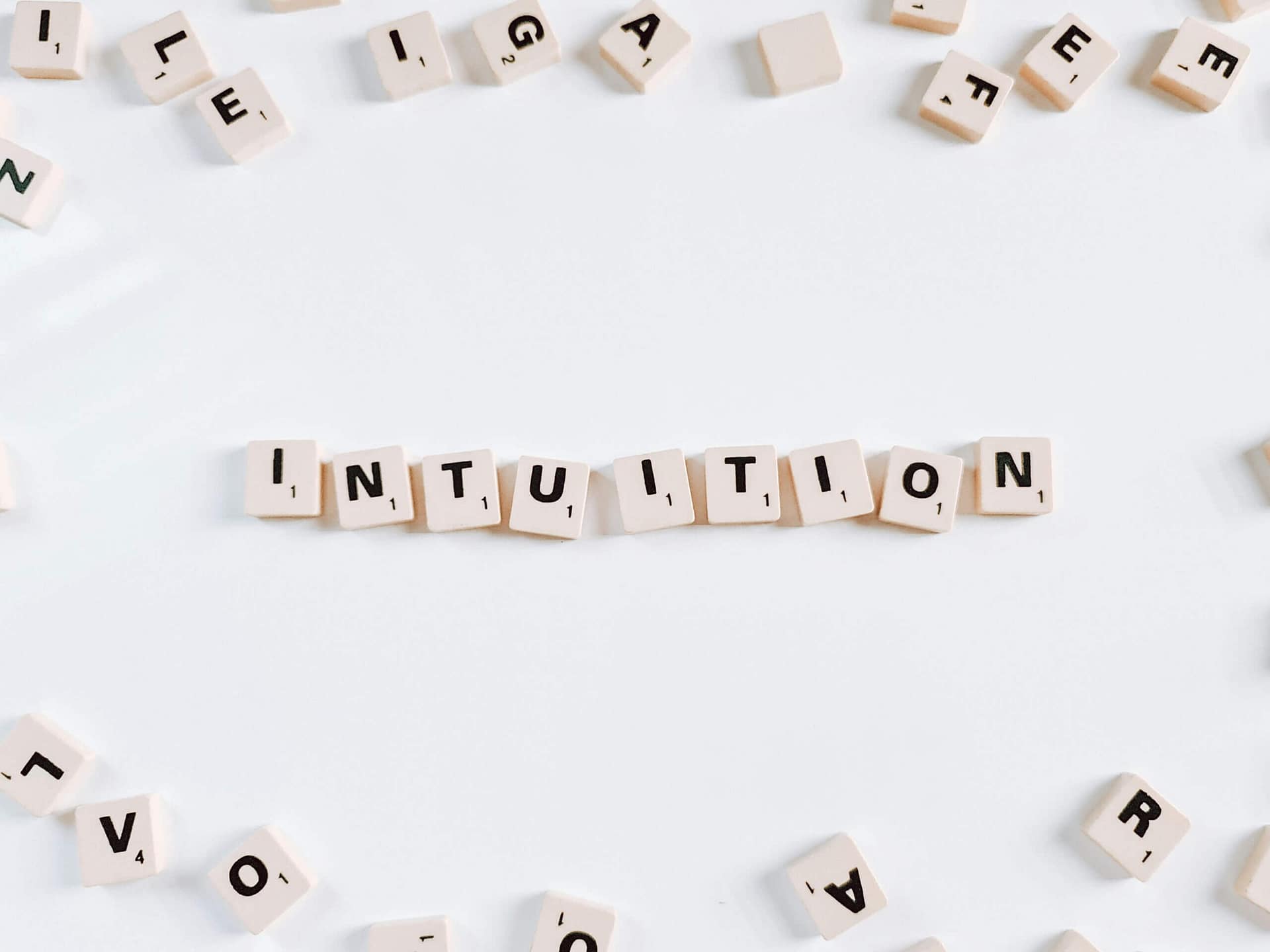 the word Intuition spelled out in Scrabble tiles surrounded by scattered letters