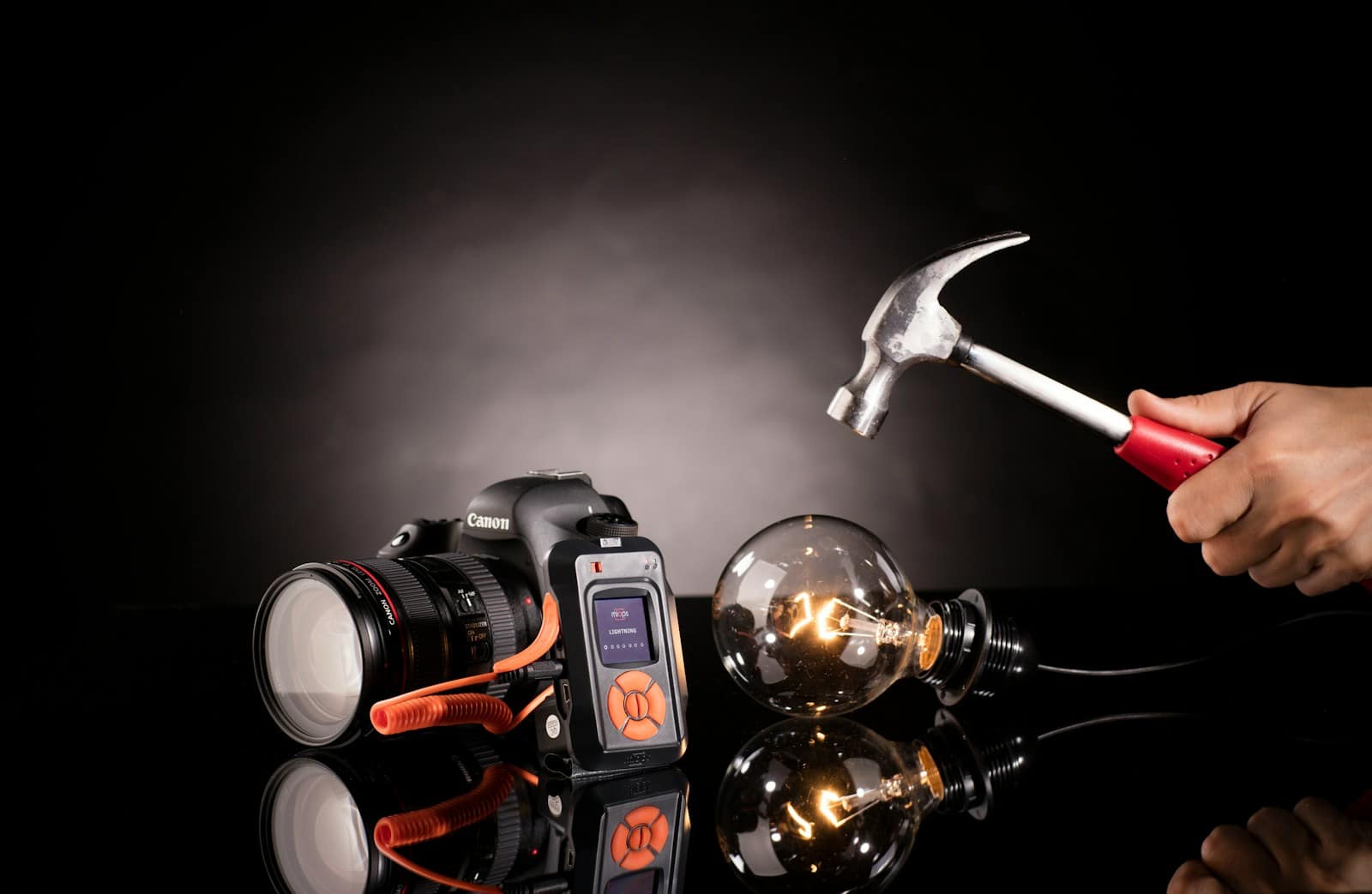 person holding claw hammer beside bulb and DSLR camera