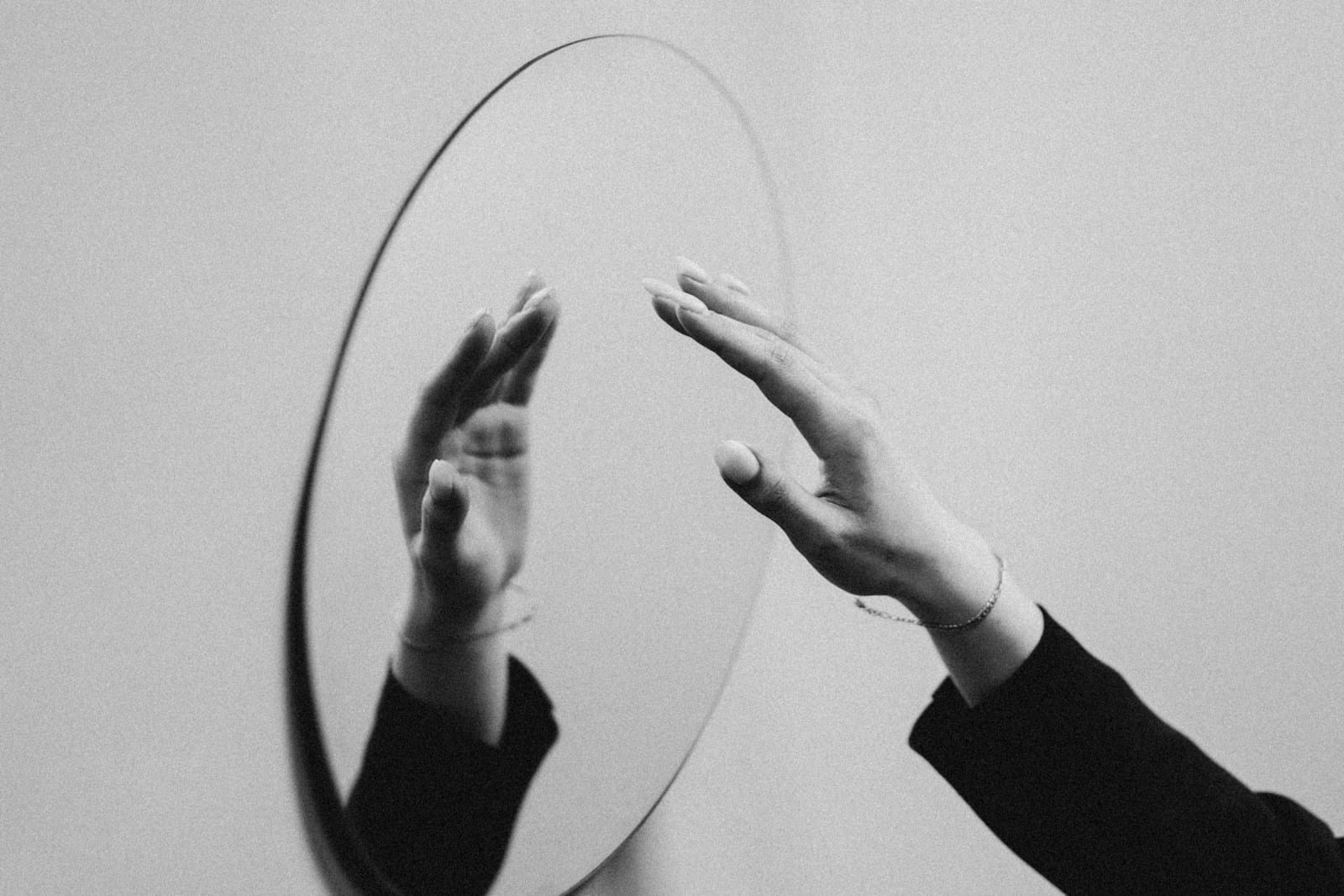 A hand reaching toward its reflection in a mirror, symbolising self-discovery through the Enneagram and tarot.