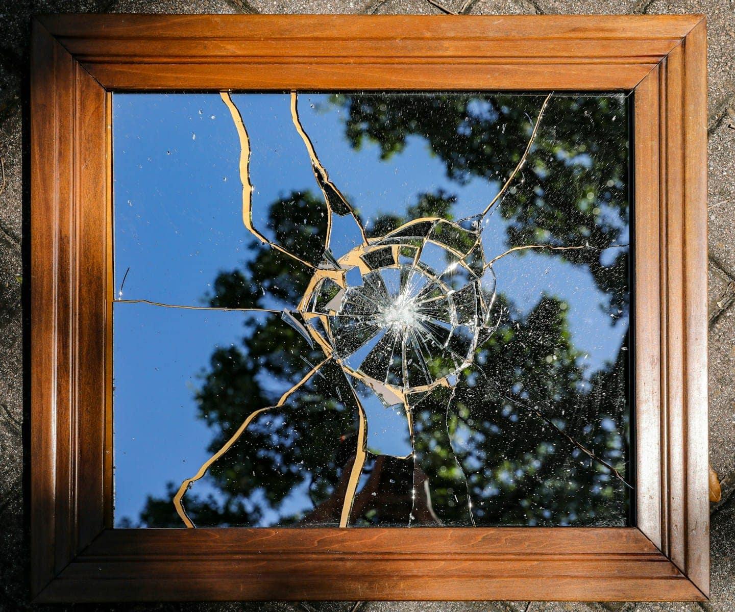 Broken mirror reflecting trees and sky, symbolising the disconnection and confusion often felt by Type Nine before self-awareness begins.