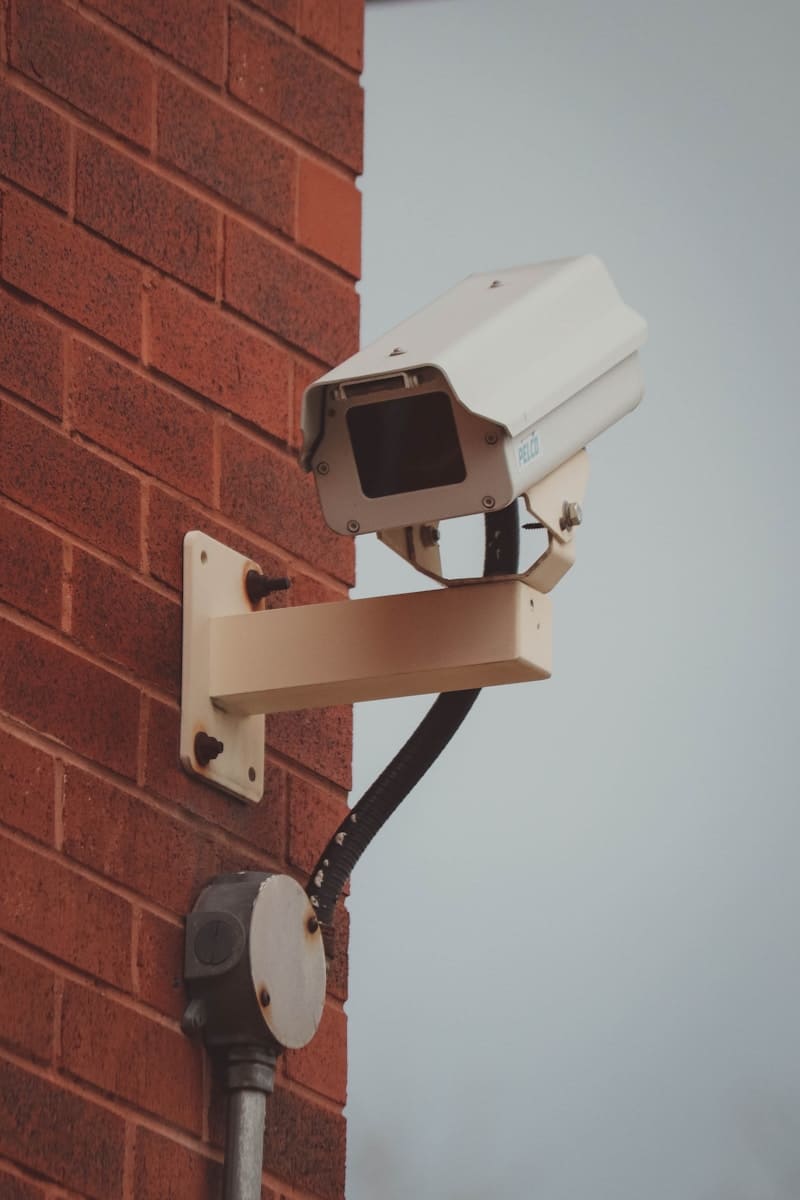 Surveillance camera on a brick wall symbolising tarot reader red flags, especially spying on third parties without consent.