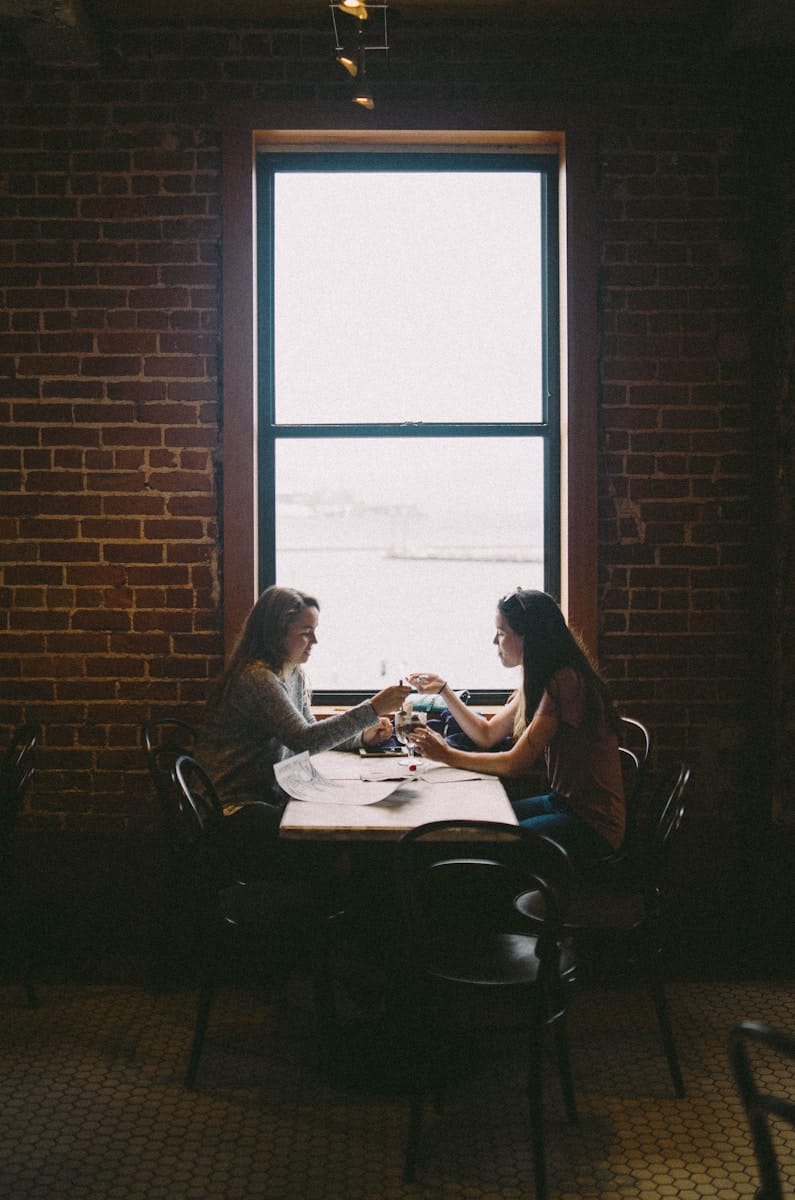 “Two people sitting across from each other at a table, representing a tarot reader and client setting boundaries and discussing spiritual work and money