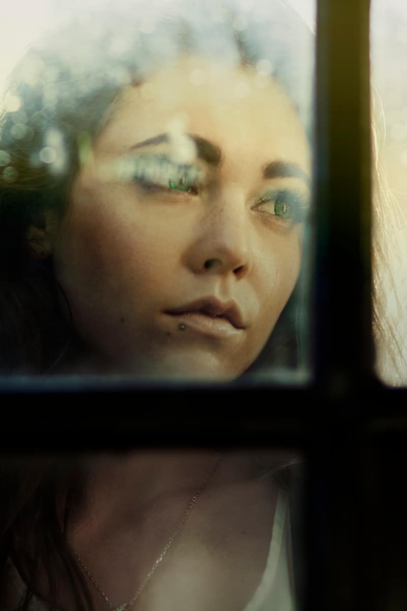 Thoughtful woman looking out of a window, reflecting on life changes and seeking clarity — a quiet moment of guidance from tarot and emotional insight.