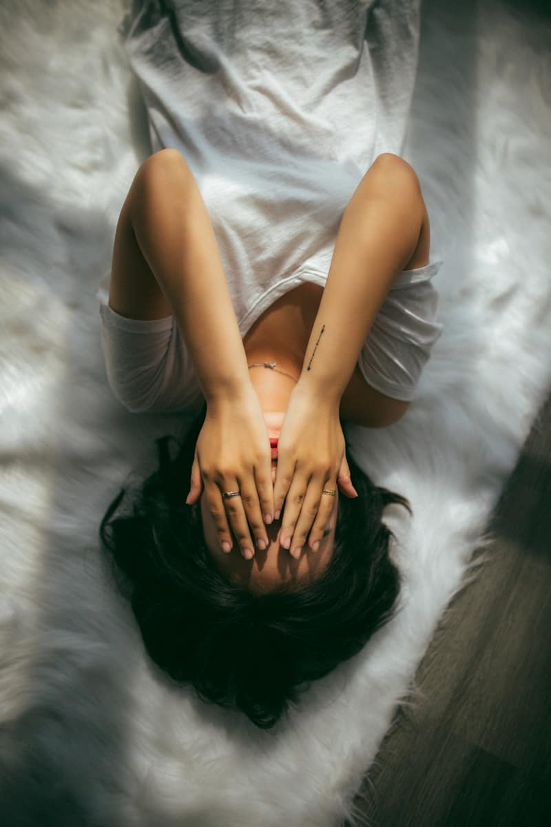 Person lying on the floor with hands covering their face, representing burnout from emotional labour and the cost of underpaid spiritual work