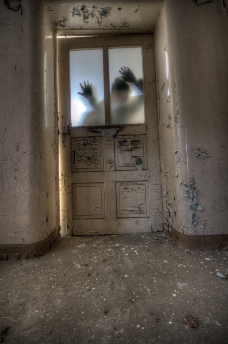 Disturbing image symbolising how to spot a fake tarot reader, showing a shadowy figure behind a broken door in an eerie, abandoned hallway.