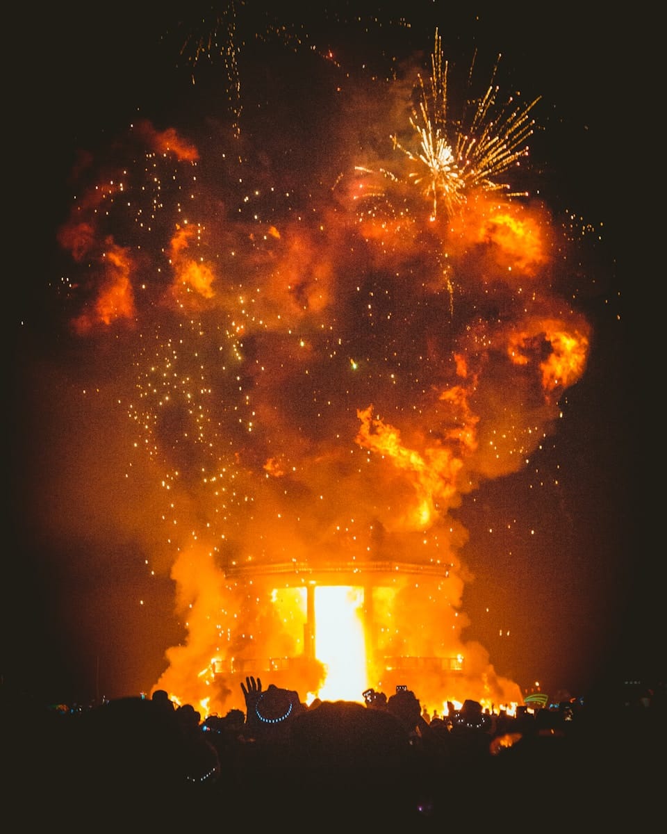 A dramatic explosion of fire and sparks lighting up the night sky during a large burn event, symbolising emotional overwhelm, collapse, and the intensity of a personal breakdown.
