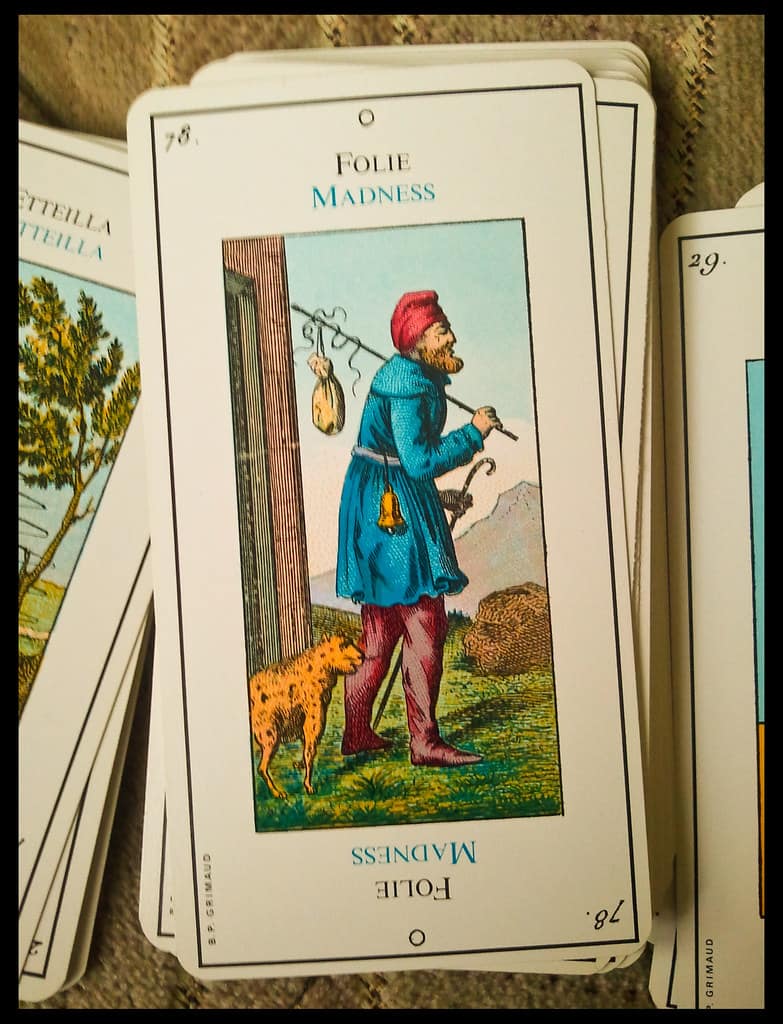 Card from the Grand Etteilla tarot deck titled ‘Folie’ or ‘Madness’, showing a reversed figure with a red hat and a leopard, illustrating early esoteric tarot symbolism.